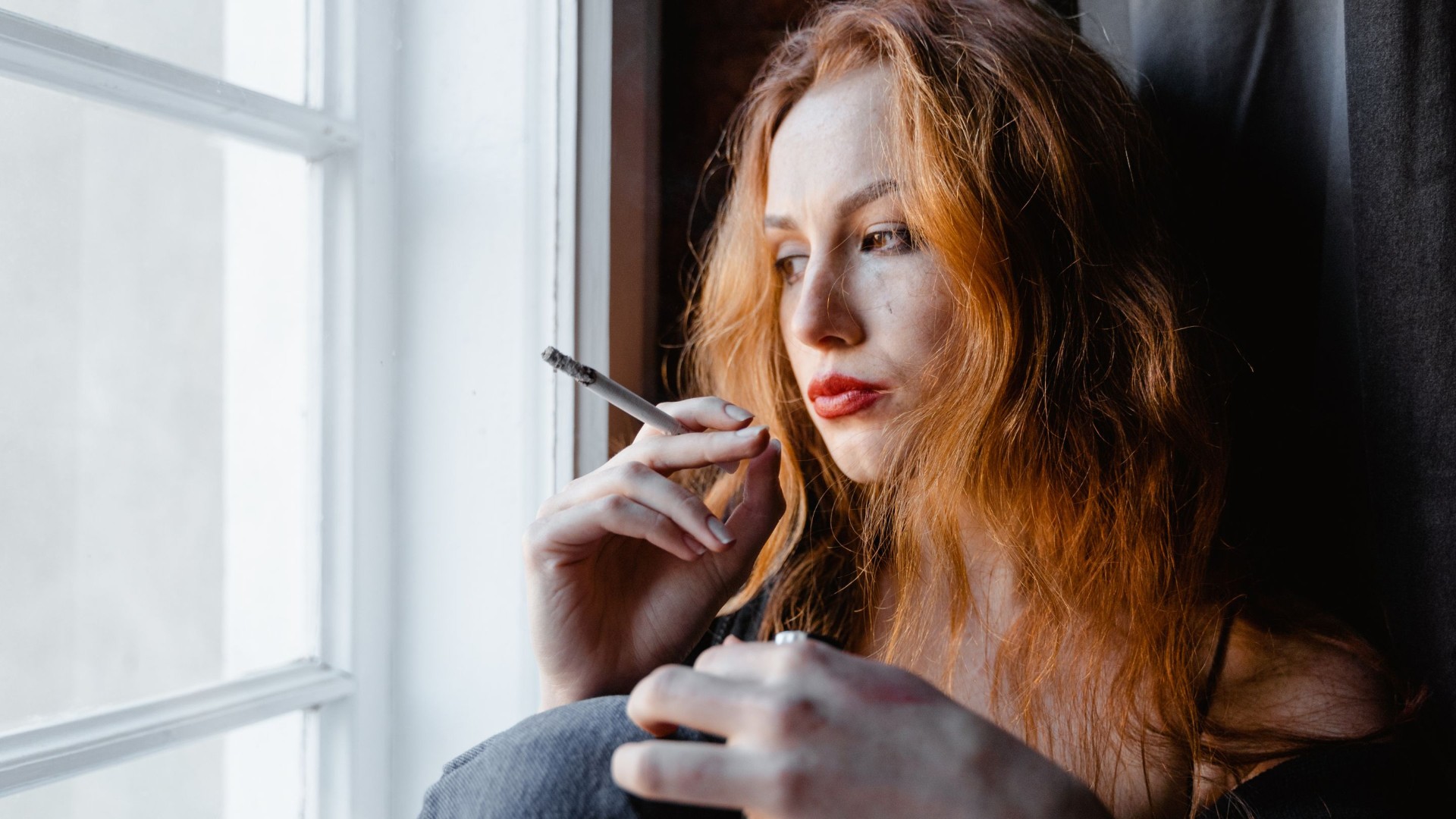 Donna pensierosa che fuma una sigaretta vicino alla finestra